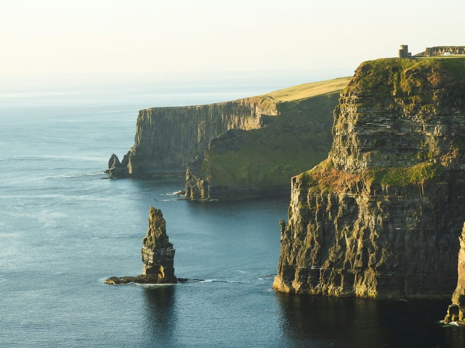 Late sunlight on the Cliffs of Moher, with a sea stack rising from calm water below