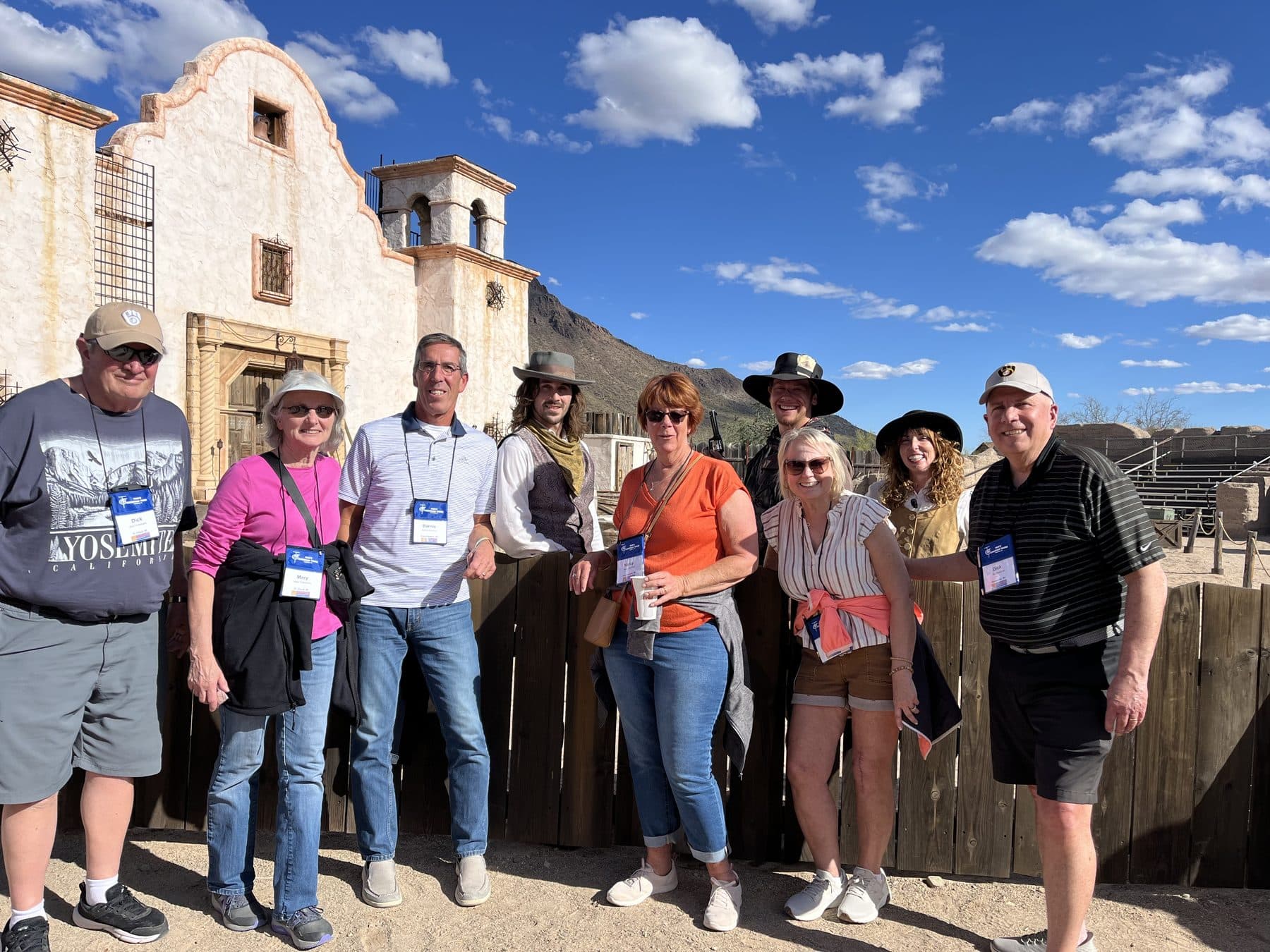 A Tom's Christian Tours group smiling with costumed cowboys outside an old Western mission