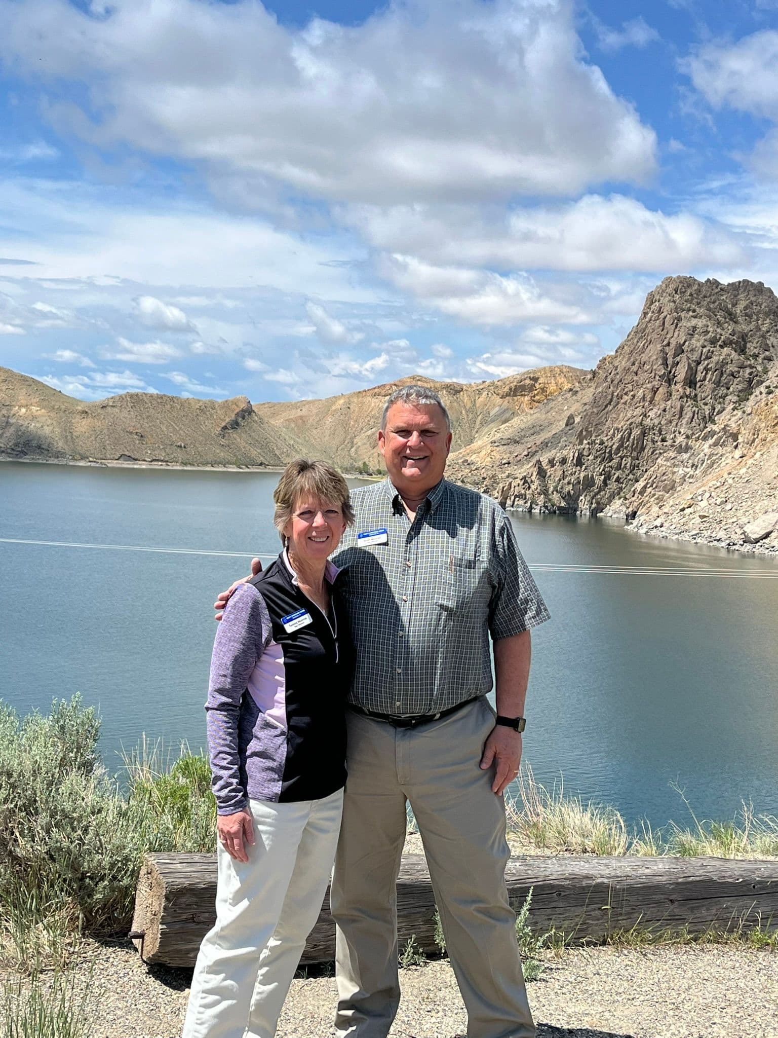 Scott and Tammy Monroe arm in arm beside a mountain lake, both wearing Tom's Christian Tours name badges